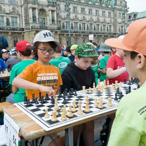 Zwei Kinder beim Schaf spielen. Im Hintergrund ganz viele Kinder die ebenfalls Schach spielen