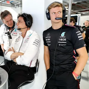 Mick Schumacher in der Garage von Mercedes mit einem Headset auf. Im Hintergrund unterhält sich Teamchef Toto Wolff mit Markus Schäfer.