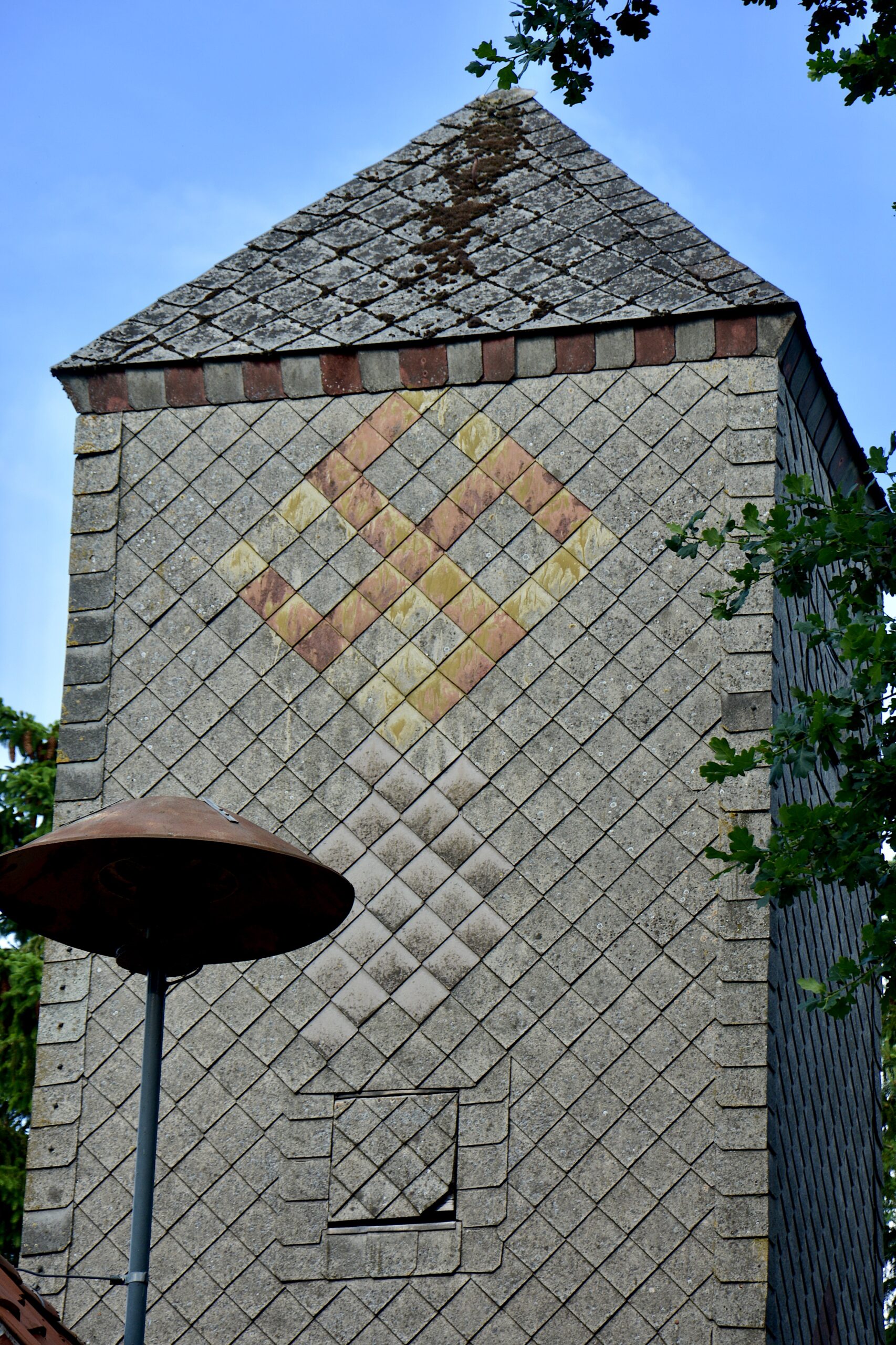 Das Hakenkreuz, gelb-orange auf grauen Schindeln, am höchsten Turm in Hönau-Lindorf