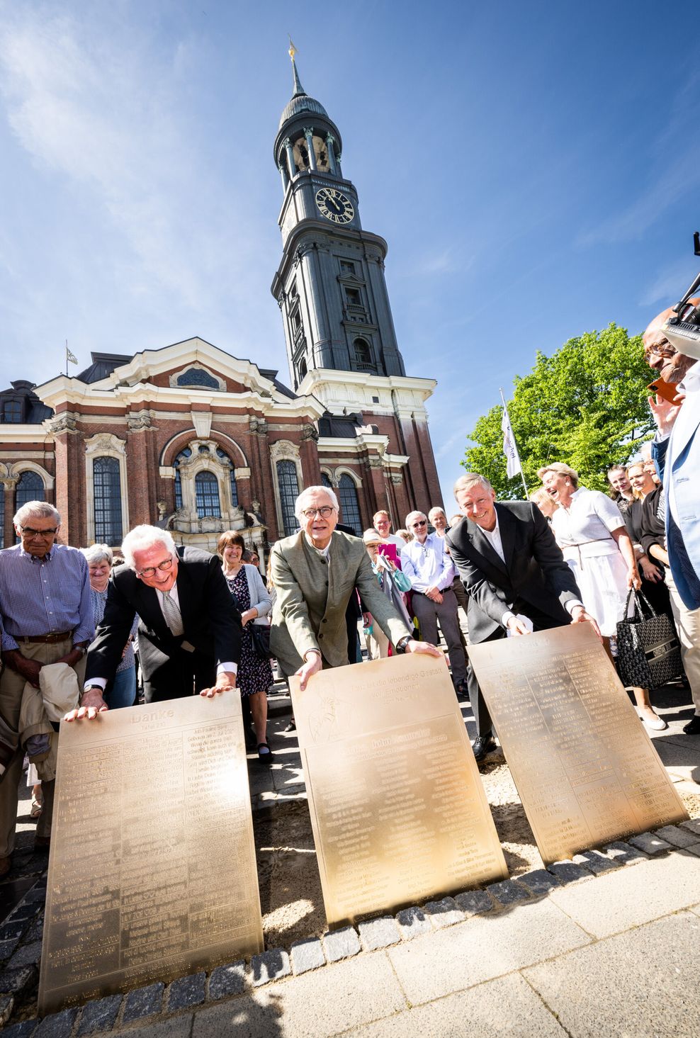 Die drei Männer vorne, hinten weitere Menschen, noch weiter hinten die Kirche