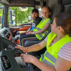 Die Viertklässlerinnen Frieda (Mitte) und Amina bekommen vom angehenden Lkw-Fahrer Adem Okan die Spiegel und die Mechanik des Lkw erklärt.