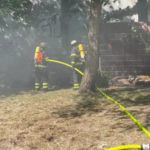 Feuerwehrleute löschen einen kleinen Brand auf einer Wiese.