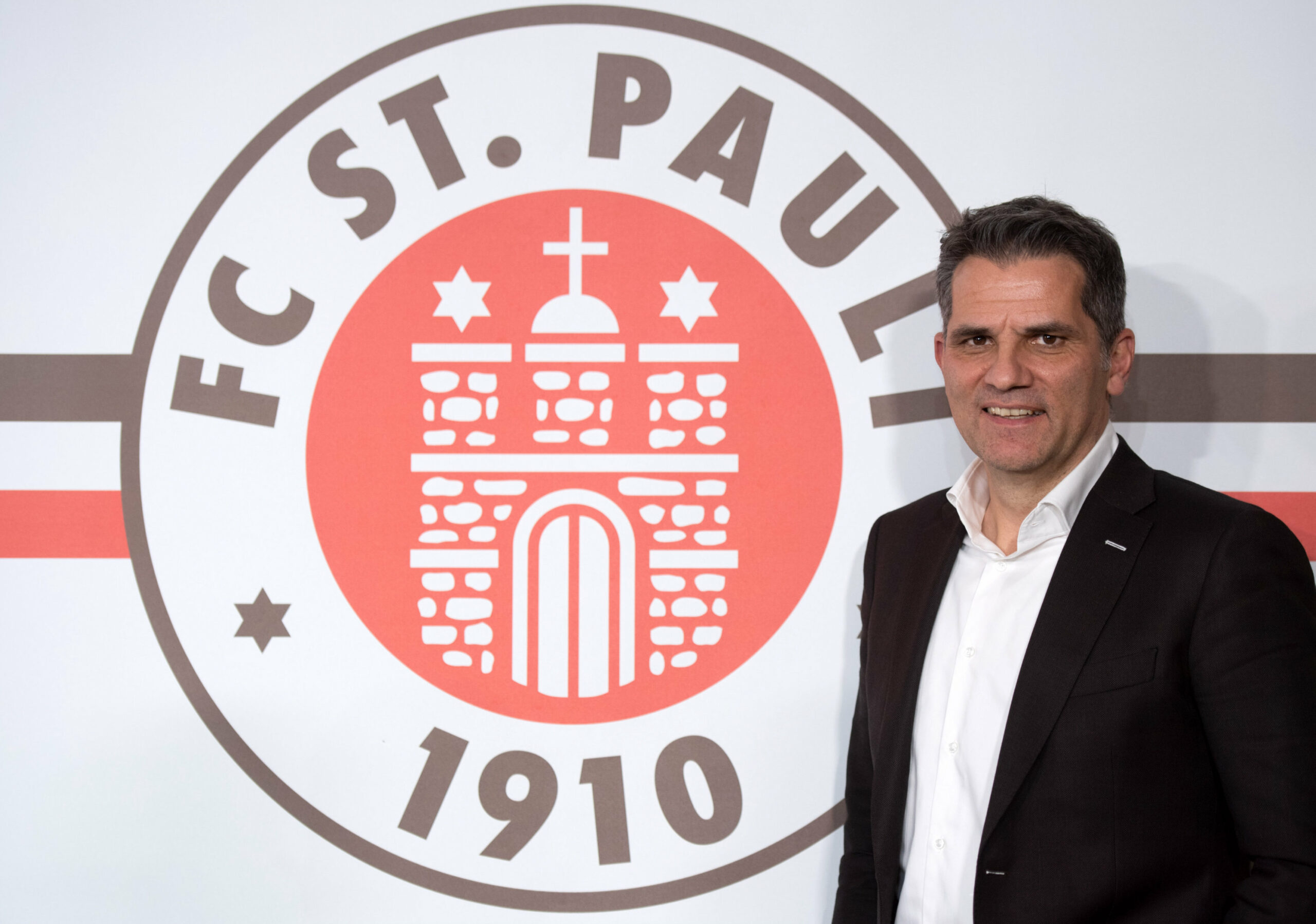 St. Paulis Vizepräsident Carsten Höltkemeyer posiert vor dem St. Pauli-Logo.