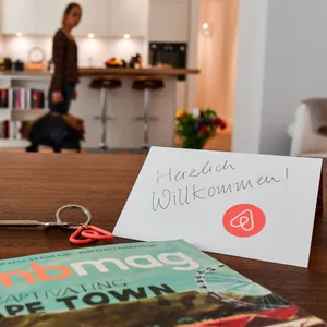 Ein Schlüssel mit einem Airbnb-Anhäger, ein Airbnbmag-Magazin und eine Herzlich-Willkommen-Karte liegen in der Wohnung eines Airbnb-Gastgebers