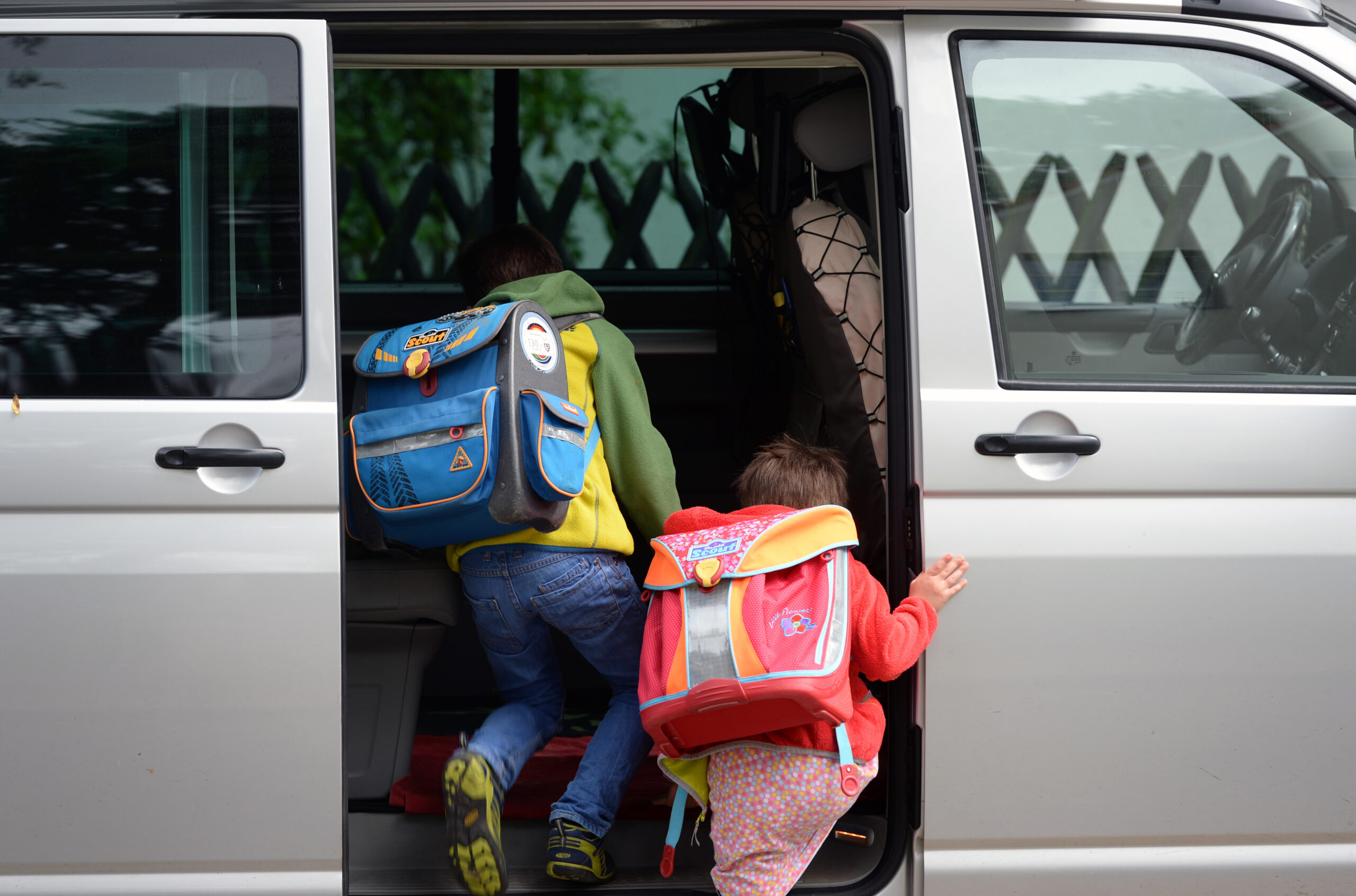 Zwei Schulkinder mit Ranzen steigen in ein Auto