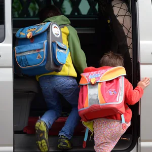 Zwei Schulkinder mit Ranzen steigen in ein Auto