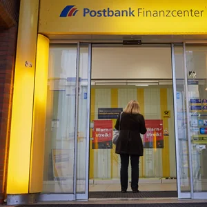 Eine Kundin steht vor einer Postbank-Filiale.