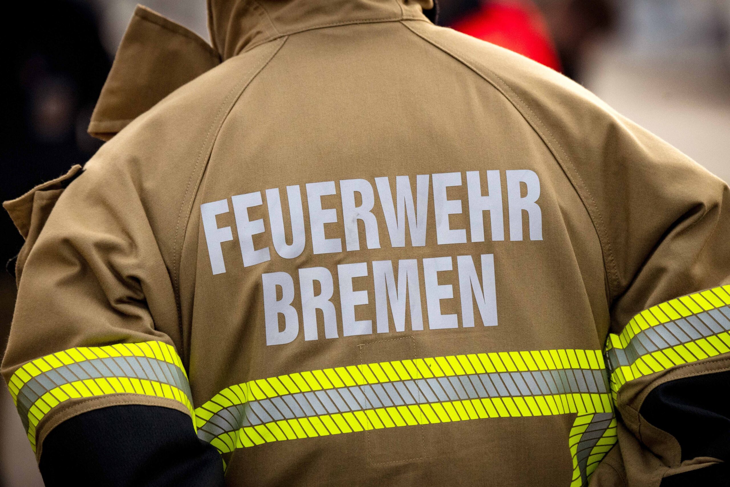 Einsatzkraft der Bremer Feuerwehr von hinten, mit brauener Feuerwehrjacke mit Aufschrift (Feuerwehr Bremen)