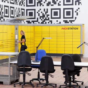 Eine DHL-Pakstation steht vor einer Wand mit einem großen QR-Code.