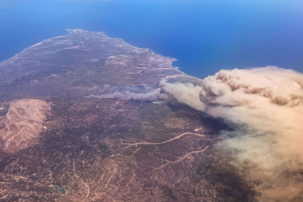 Die Insel Rhodos von oben zu sehen. Über ihr eine riesige Rauchschwarde