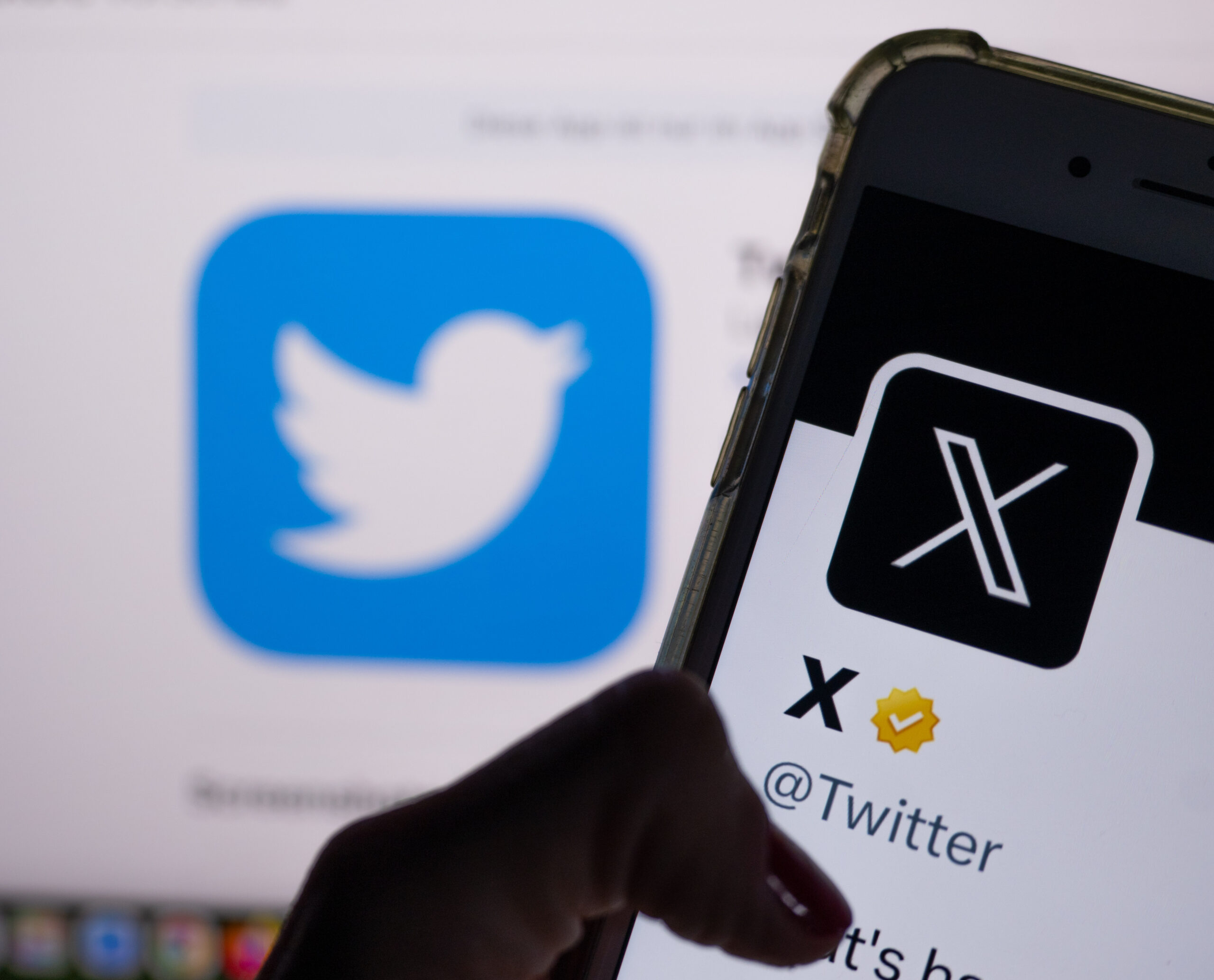 Das offizielle Profil von Twitter auf dem Bildschirm eines Smartphones ist der weiße Buchstabe X auf schwarzem Hintergrund zu sehen, während im Hintergrund das bisherige Logo des Kurznachrichten-Dienstes Twitter angezeigt wird