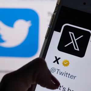 Das offizielle Profil von Twitter auf dem Bildschirm eines Smartphones ist der weiße Buchstabe X auf schwarzem Hintergrund zu sehen, während im Hintergrund das bisherige Logo des Kurznachrichten-Dienstes Twitter angezeigt wird