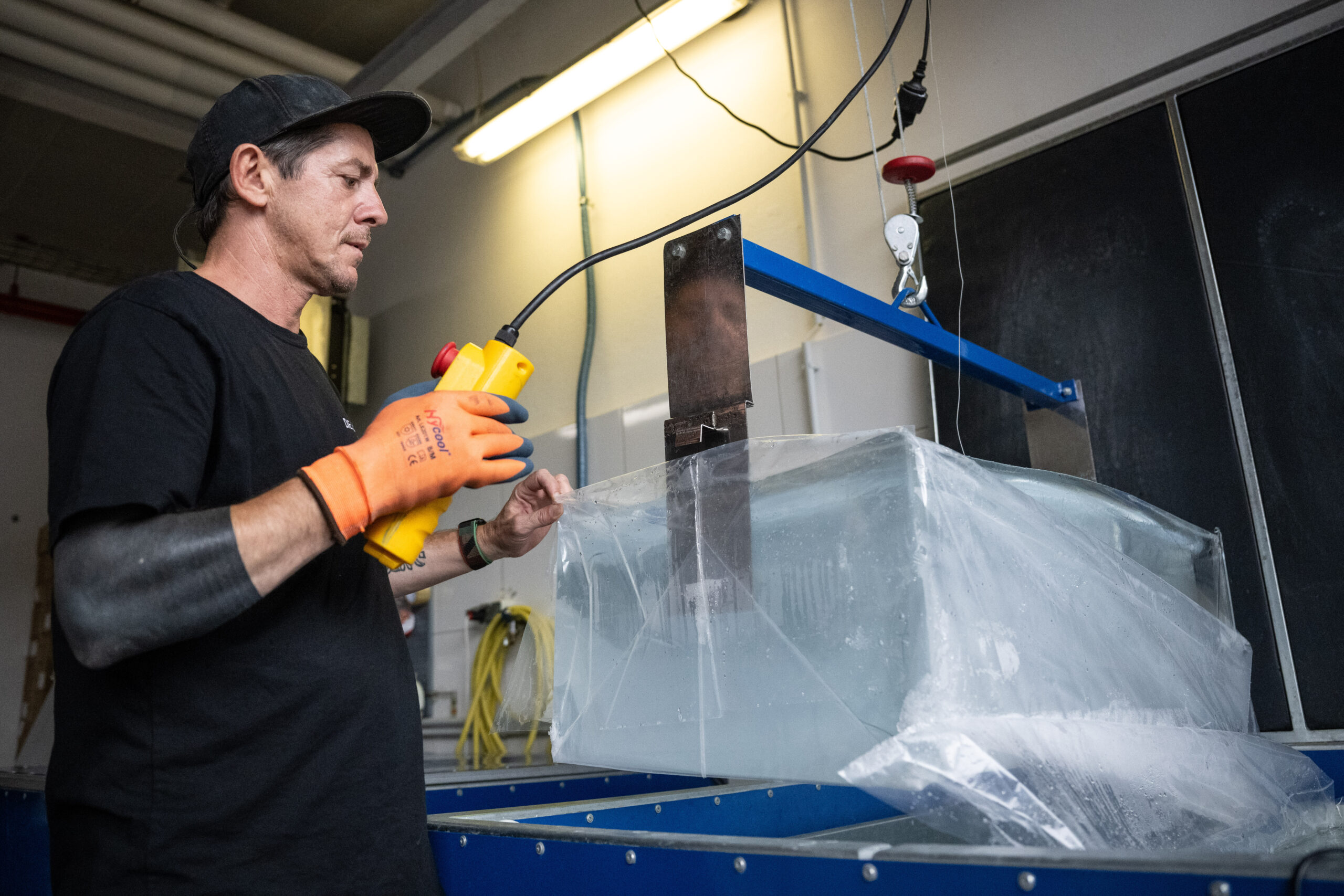 Sezgin Albayrak hebt in seiner Berliner Eisfabrik mit Hilfe eines Krans einen Eisblock aus der Form.