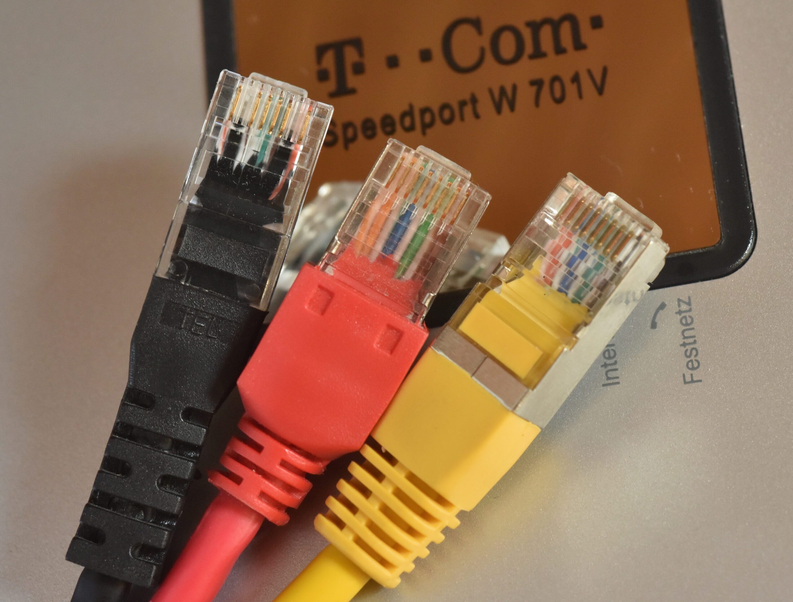 Drei RJ45-Netzwerkstecker liegen vor einem Internet-Router der Deutschen Telekom. (Symbolbild)