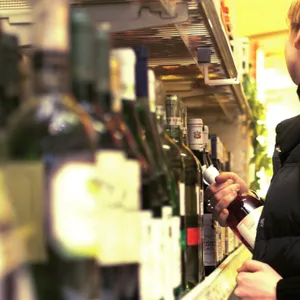 Supermarktregal mit Alkohol-Flaschen. Mensch in schwarzer Kleidung versteckt eine Flasche in seiner Jacke.