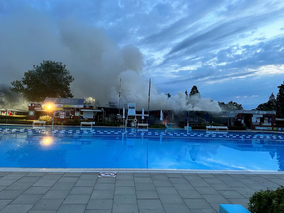 Freibadbecken, Gebäude dahinter mit starker Rauchentwicklung.