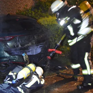 Einsatzkräfte der Feuerwehr löschen ein brennendes Auto.