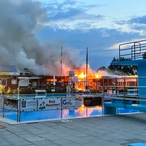 Freibad-Backen mit Sprungturm, Gebäude dahinter steht in Flammen.