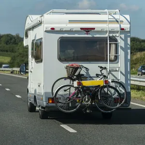 Ein Wohnmobil auf einer Schnellstraße von hinten. Im Hintergrund grüne Wiesen, Bäume und Windräder.