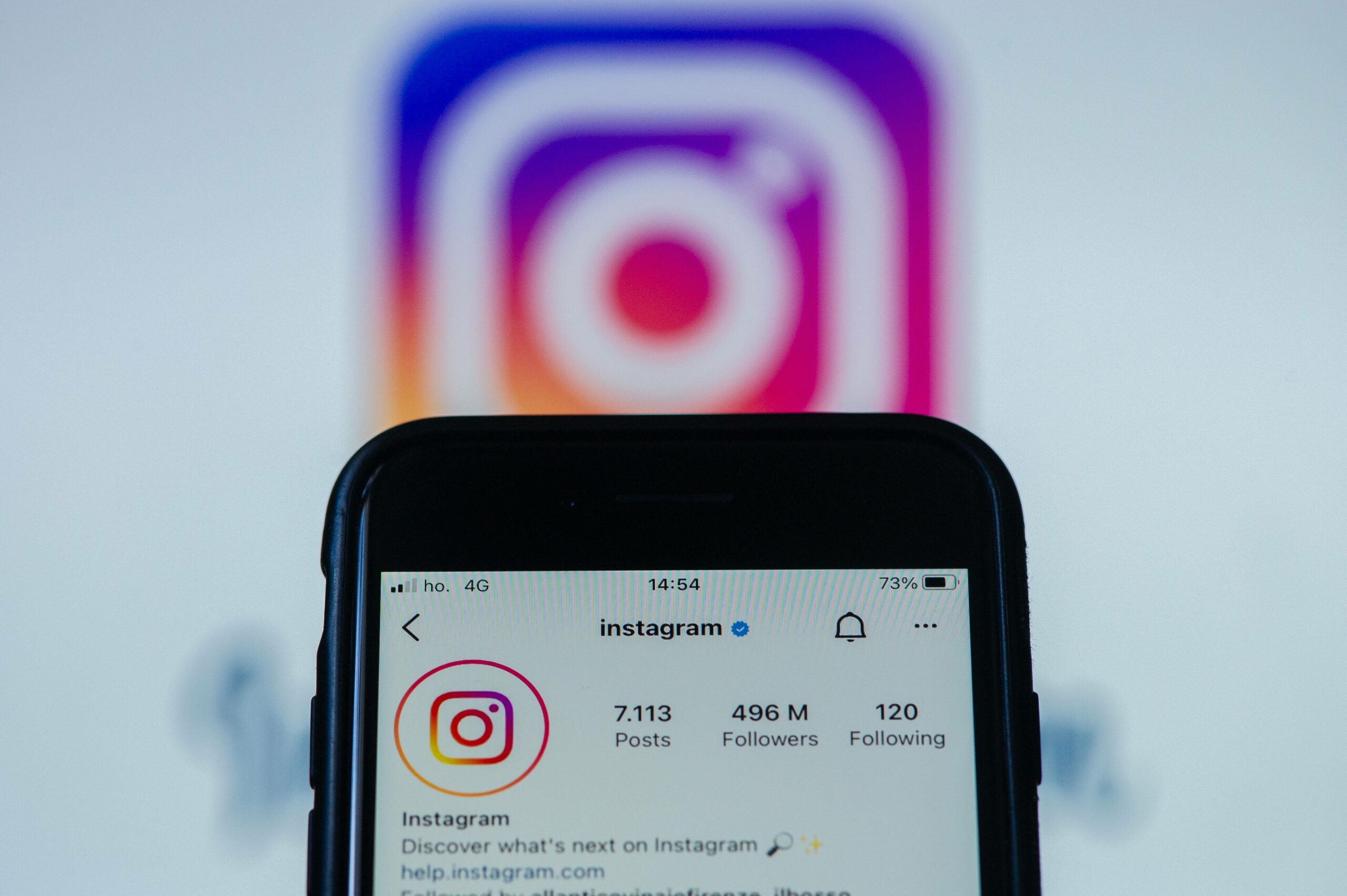 Im Hintergrund ist ein unscharfes Instagram-Logo, davor hält jemand ein Smartphone mit der geöffneten Instagram-App in die Kamera.