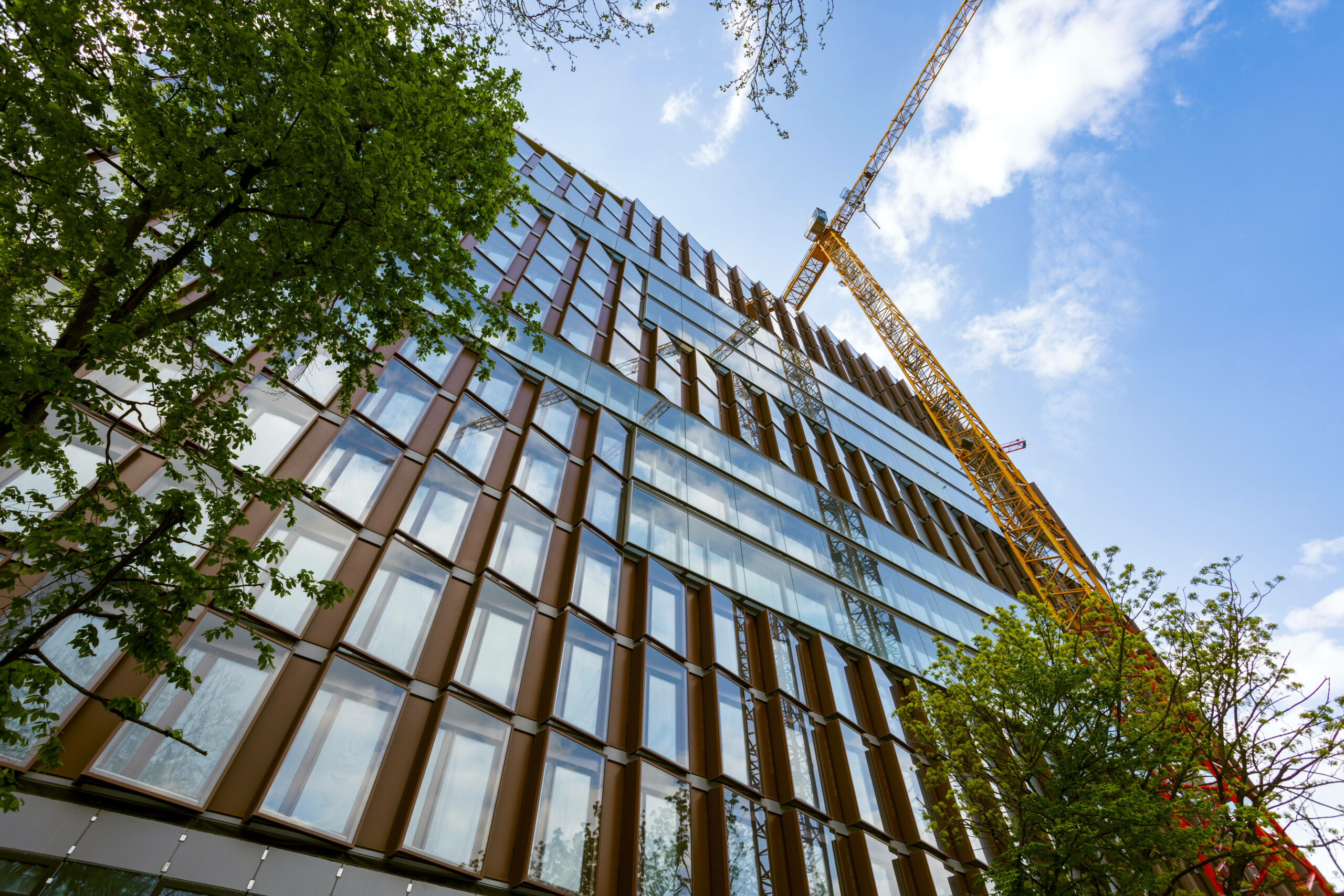 Fassade eines Bürogebäudes mit vielen Fenstern aus der Froschperspektive mit einem Kran daneben.
