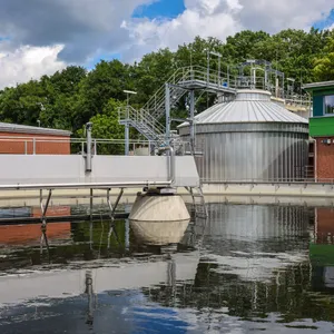 Ein Klärbecken im Vordergrund mit einem höheren Klärwerkgebäude im Hintergrund.