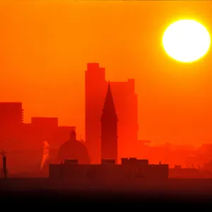 Die Skyline einer Stadt, darüber steht die gleißend helle Sonne als großer Ball.