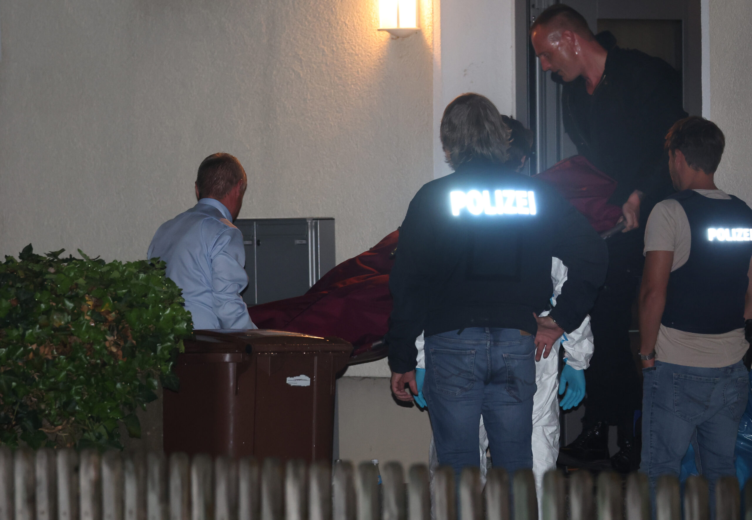 Eine Leiche wird aus dem Mehrfamilienhaus bei Augsburg getragen.