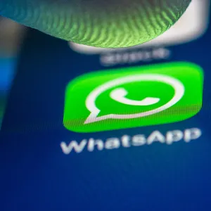 Ein Smartphone-Display in Nahaufnahme, ein Finger schwebt knapp über dem WhatsApp-Symbol.