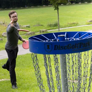 Junger Mann wirft Frisbee auf Disc-Golf-Korb.