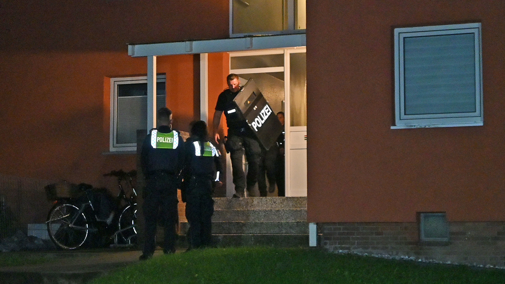 Polizisten vor dem Haus, in dem der 23-Jährige wohnt, einer trägt einen Schild