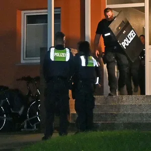Polizisten vor dem Haus, in dem der 23-Jährige wohnt, einer trägt einen Schild