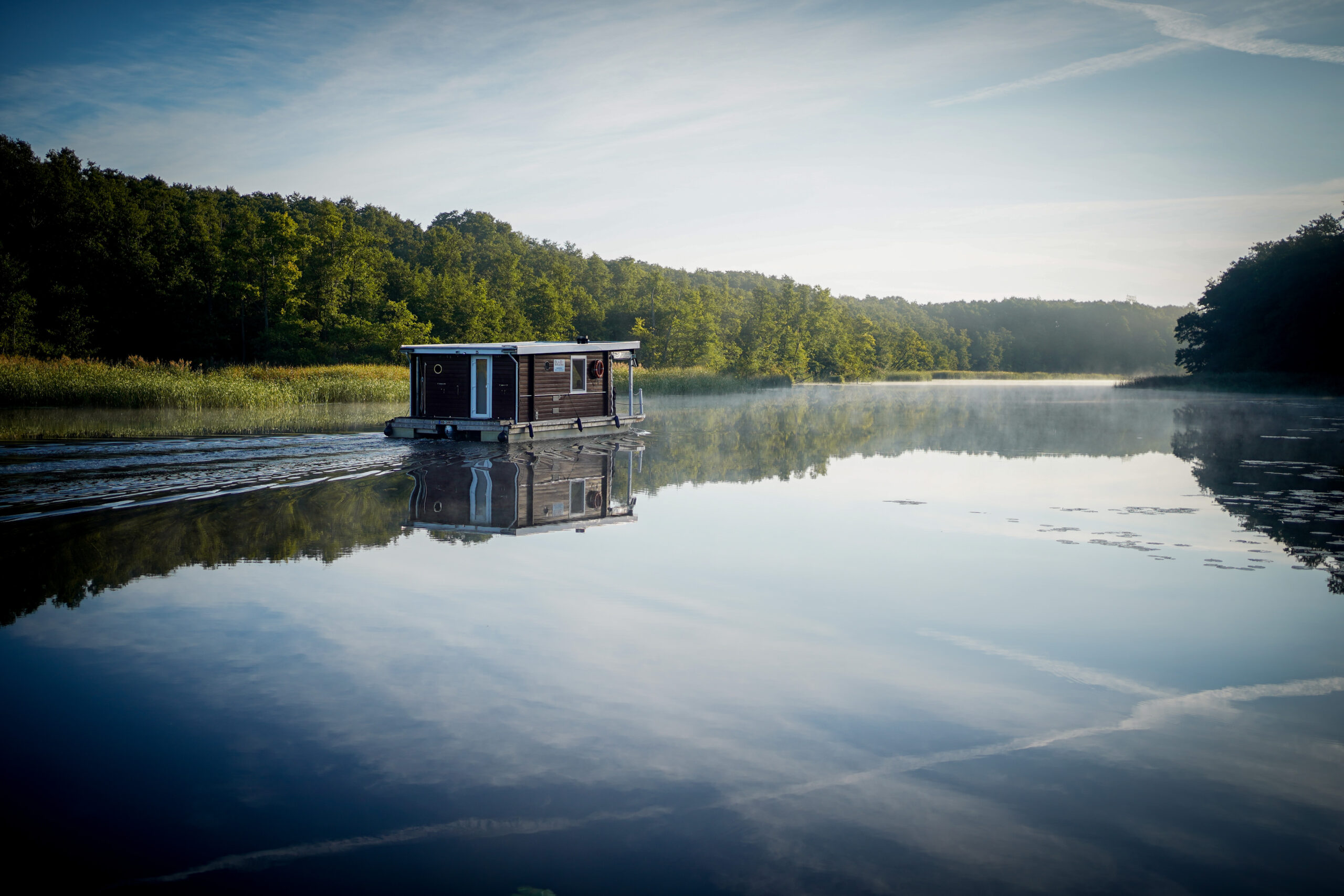 Man sieht ein Hausboot, das auf stillem Wasser treibt.