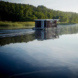 Man sieht ein Hausboot, das auf stillem Wasser treibt.