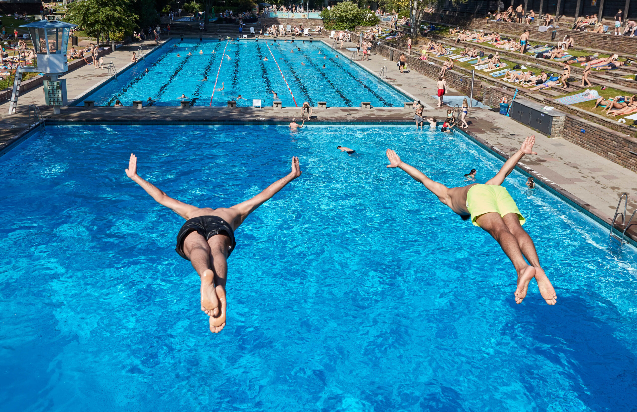 Zwei junge Männer machen einen Kopfsprung ins Schwimmbecken des Kauf-Freibades