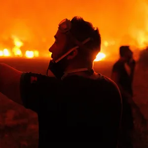 Menschen stehen am Montag am Rande von Löscharbeiten in einem Dorf in der Nähe der Stadt Alexandroupolis in Griechenland.