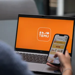 Eine Person hat die Temu-Website auf ihrem Laptop und die Temu-App auf ihrem Smartphone geöffnet.