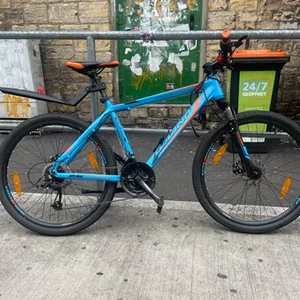Man sieht ein Mountainbike mit blauem Ramen und orangenen Akzenten an Sattel, Lenker und Gestell.