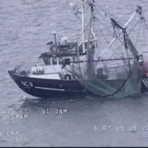 Man sieht einen Fischkutter, dessen Bug brennt und Rauch entwickelt auf dem Wasser.
