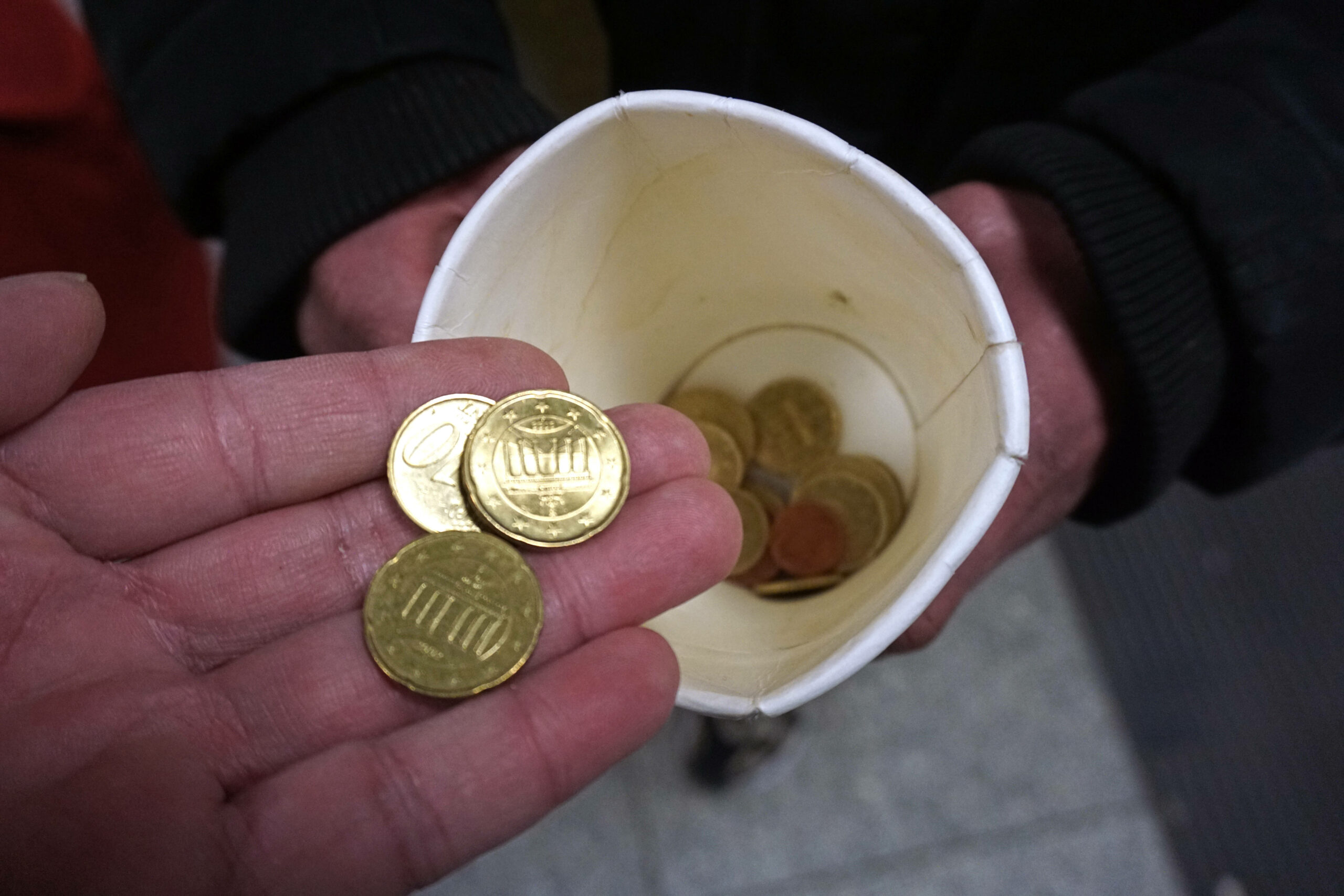 ein Benutzer Kaffeebecher mit etwas Münzgeld und eine Hand, die zwei 10-Cent-Stücke und ein 20-Cent-Stück über den Becher hält.
