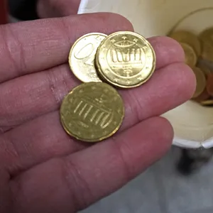 ein Benutzer Kaffeebecher mit etwas Münzgeld und eine Hand, die zwei 10-Cent-Stücke und ein 20-Cent-Stück über den Becher hält.