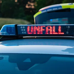Polizeiauto mit Leuchtschrift „Unfall“ auf dem Dach. Im Hintergrund ist der rötliche Abendhimmel zu sehen.