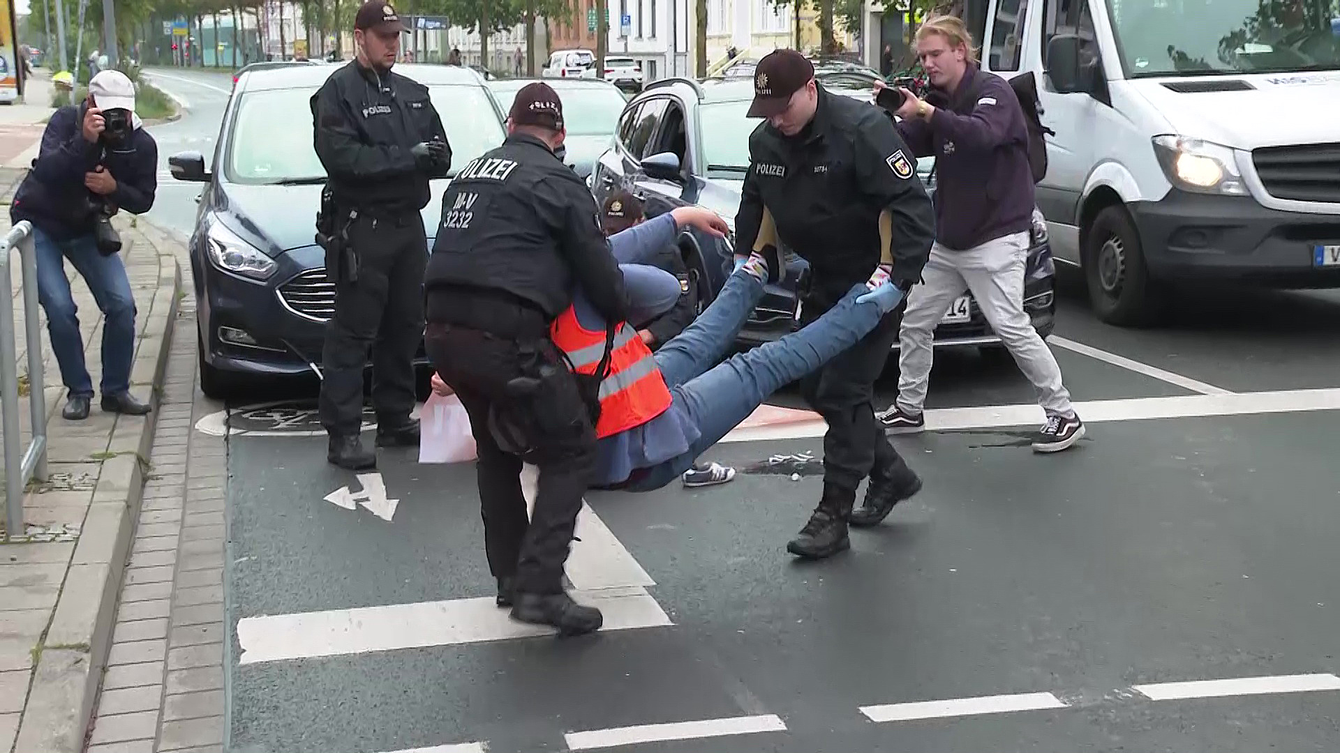 Polizisten tragen einen Klimaaktivisten der Letzten Generation in Rostock von einer blockierten Straße.