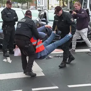 Polizisten tragen einen Klimaaktivisten der Letzten Generation in Rostock von einer blockierten Straße.