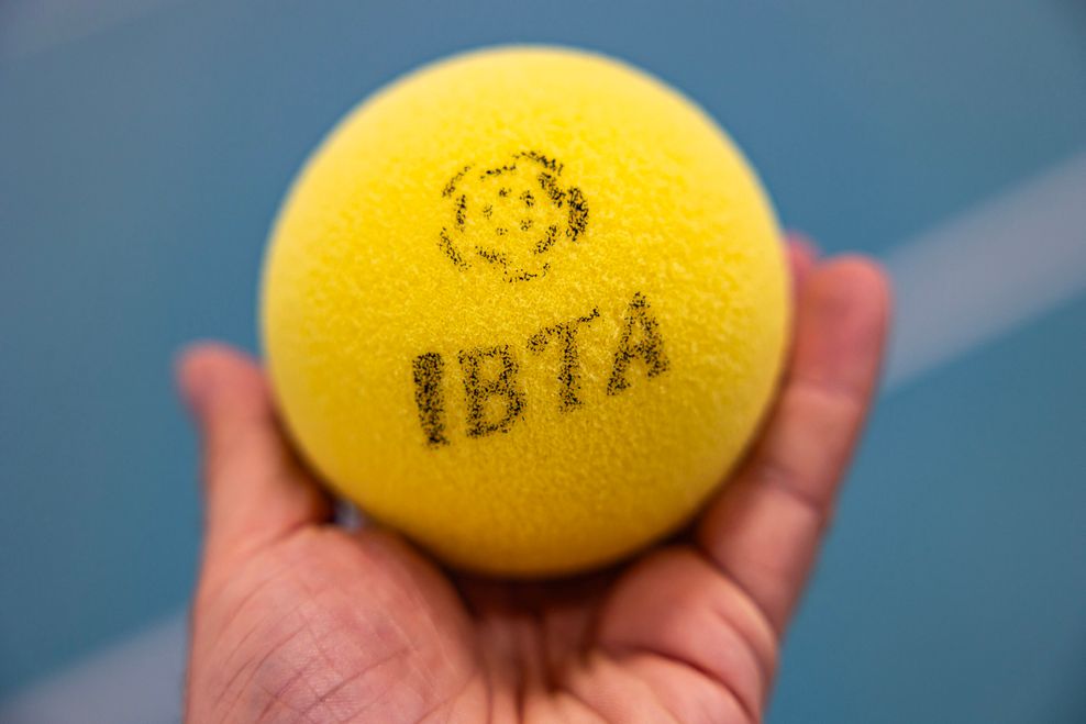 Man sieht eine Hand mit einem 10 cm großen, gelben Schaumstoff-Tennisball.