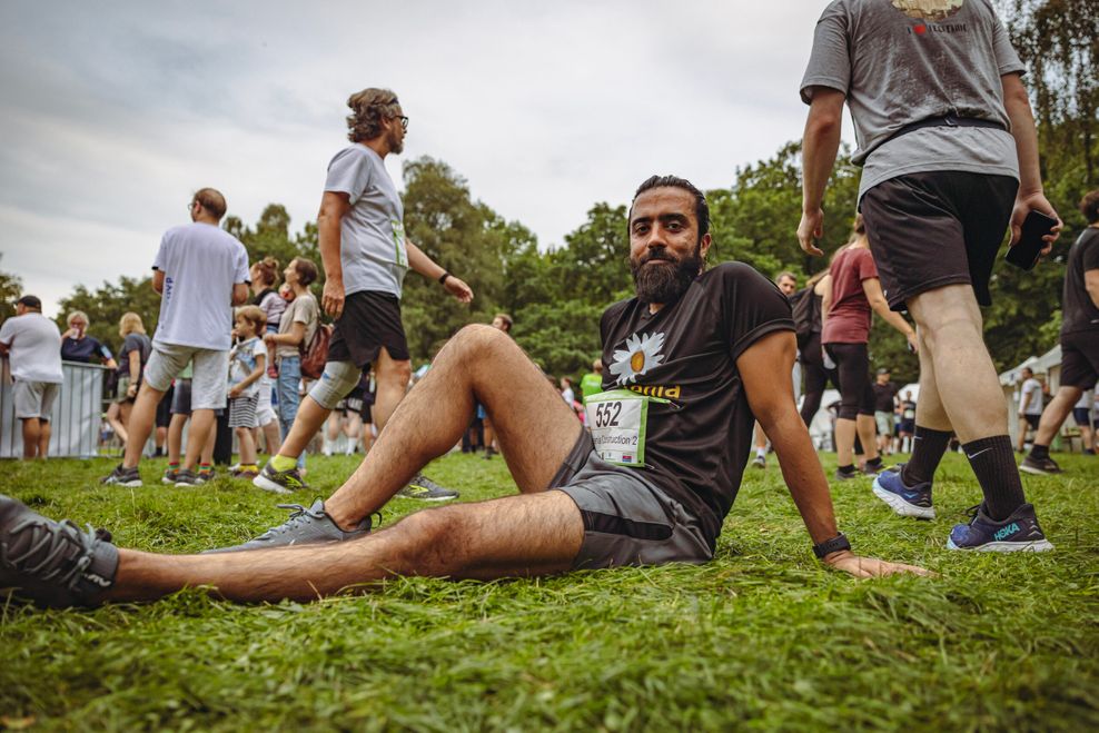 Der 37-jährige Bauingenieur Mehdi aus St. Pauli ist für die Firma „Implenia“ an den Start gegangen – und sitzt nach dem Lauf erschöpft auf dem Rasen.