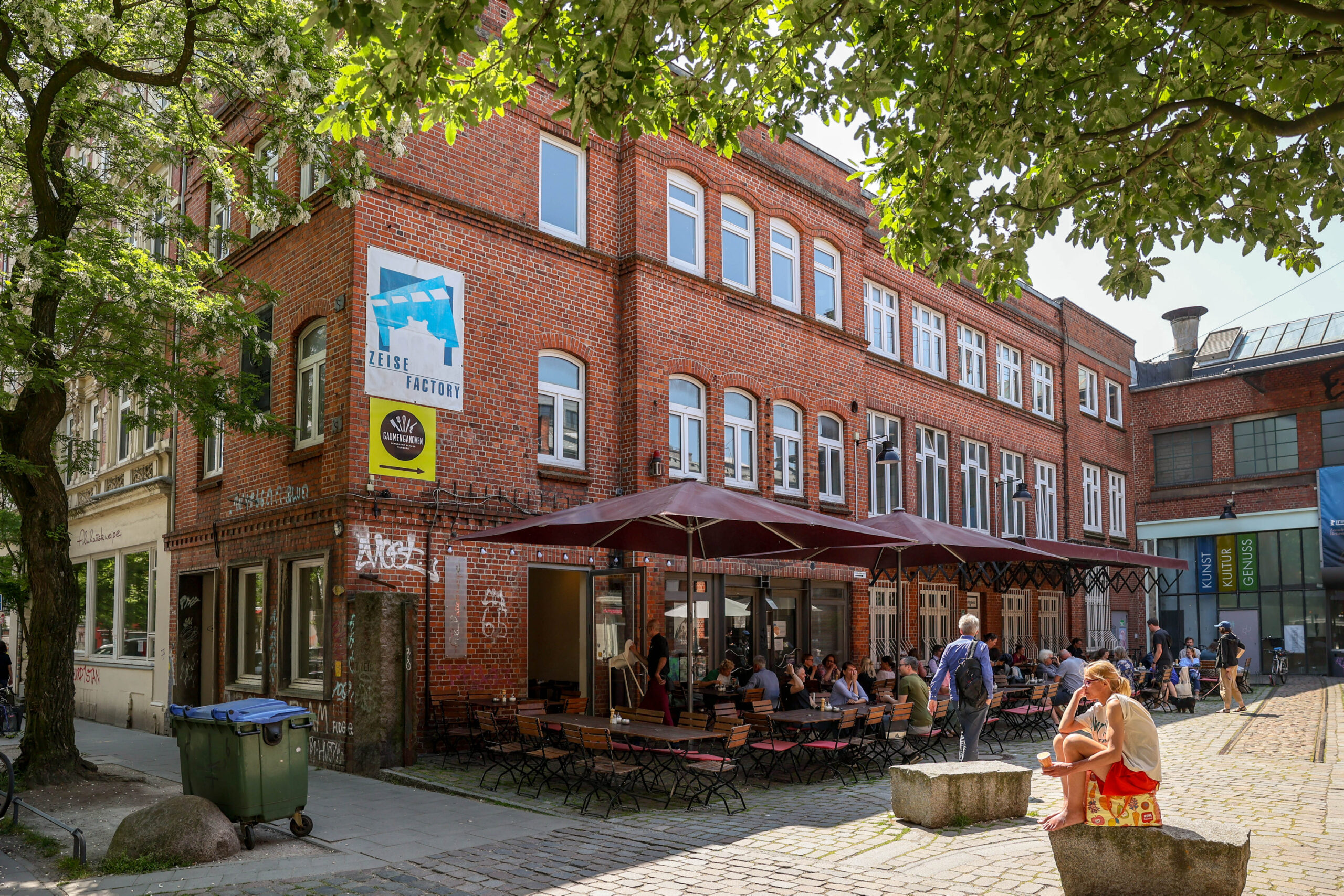 Die „Filmhauskneipe“ an der Friedensallee in Ottensen im Sommer. Zum Hof hin stehen dort Holztische und -bänke und Sonnenschirme.