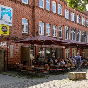 Die „Filmhauskneipe“ an der Friedensallee in Ottensen im Sommer. Zum Hof hin stehen dort Holztische und -bänke und Sonnenschirme.