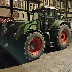 Man sieht einen Traktor geparkt vor einem Landhaus-Gebäude, es ist dunkel.