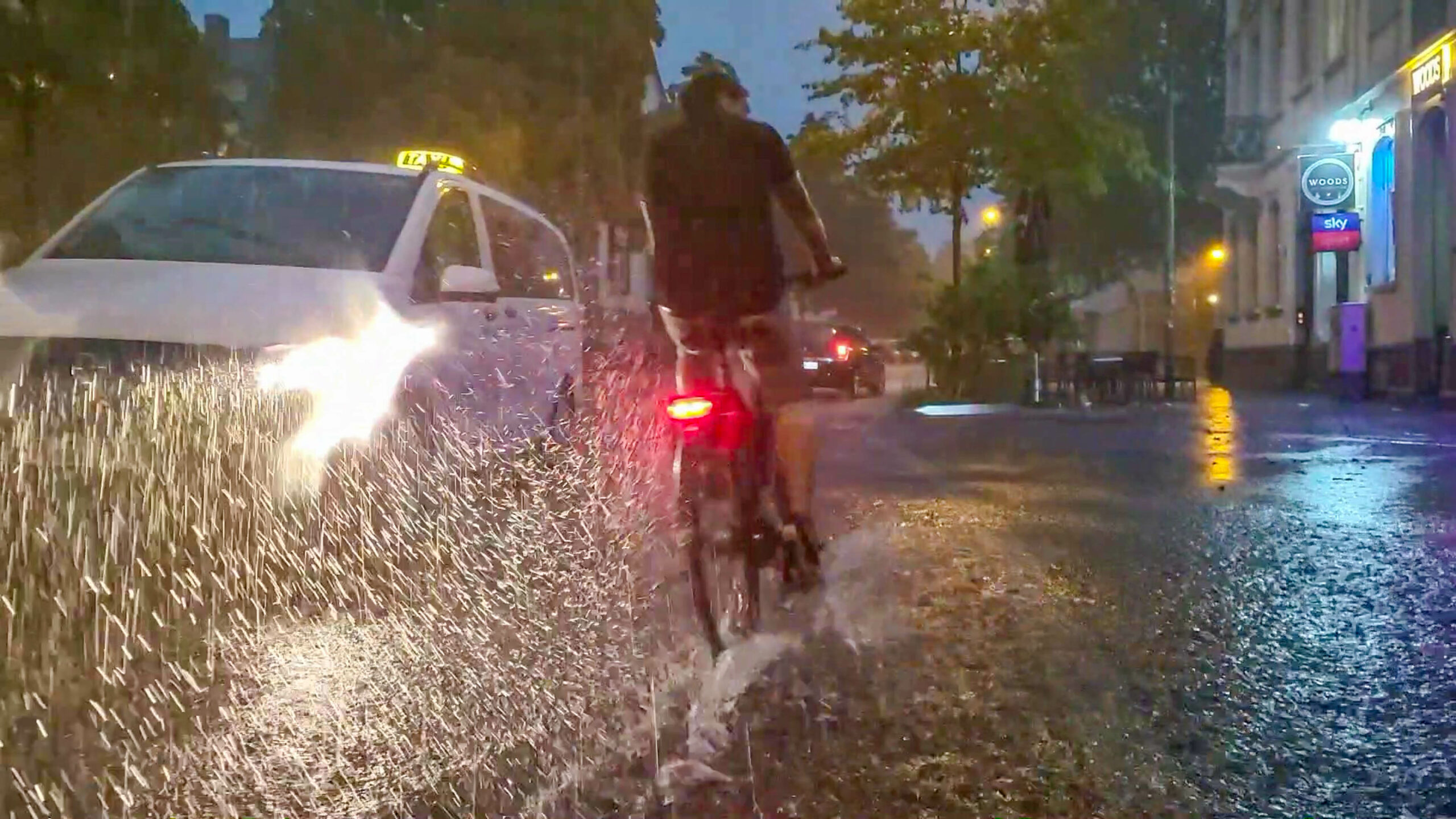 Freiburg im Breisgau: Ein Fahrradfahrer und ein Auto fahren über eine vom Regen überschwemmte Straße. Über Süddeutschland zog ein schweres Unwetter.